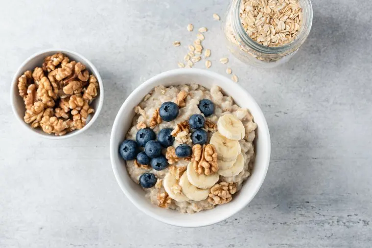 Oatmeal porridge with banana blueberry and walnuts in ceramic bowl. Top view. Grey concrete table background. Healthy eating, dieting concept