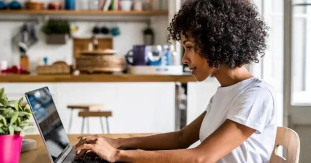 Side profile of a person sitting at a table typing into a laptop