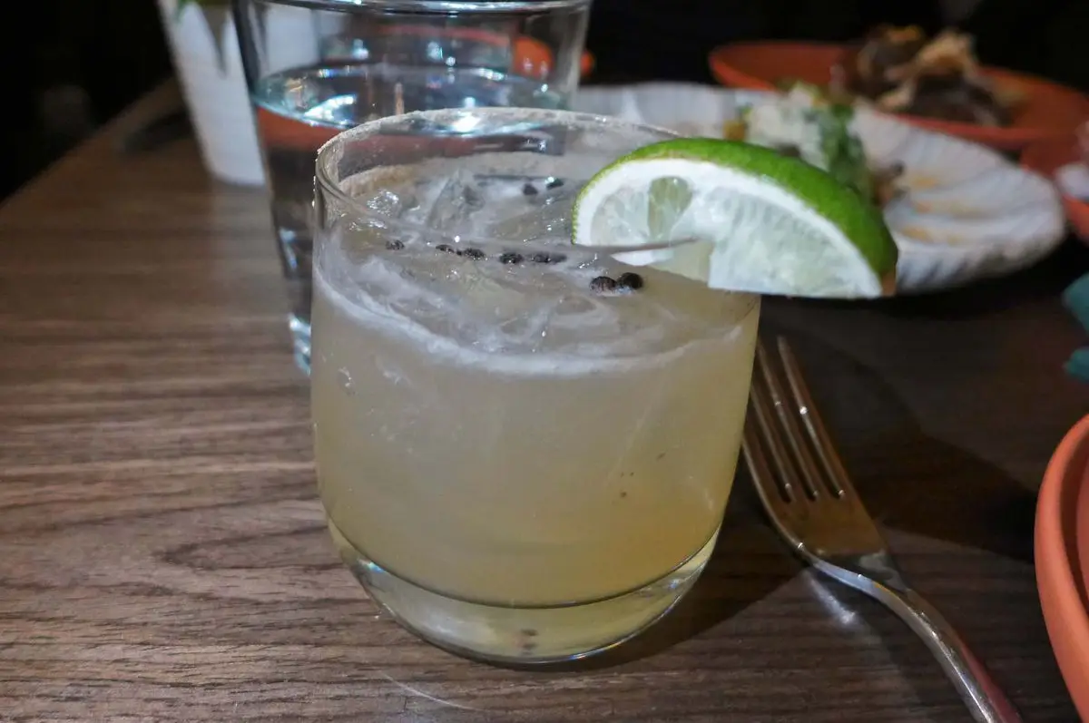 A glass with peppercorns floating on the surface and a lime wedge on the rim..