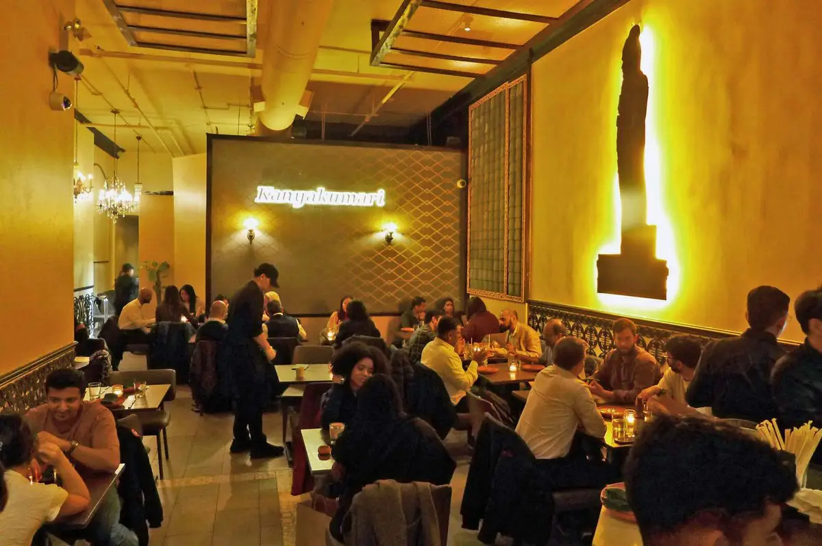 A giant Buddha on one wall with tables filled with diners down below.