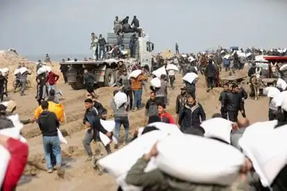 Palestinians carry bags of flour they took from a humanitarian aid truck near an Israeli checkpoint, in Gaza City, on February 19, 2024.