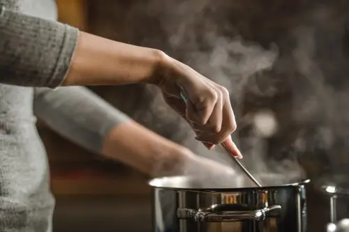 Unrecognizable woman making lunch in the kitchen and stirring soup.