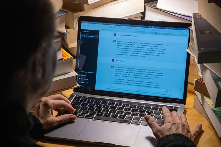 Illustration picture shows the ChatGPT artificial intelligence software being used on a laptop surrounded by books.