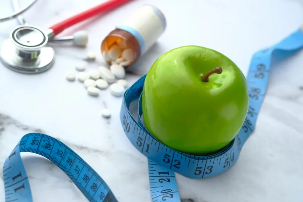 Green apple with measuring tape with pills and medicine on table