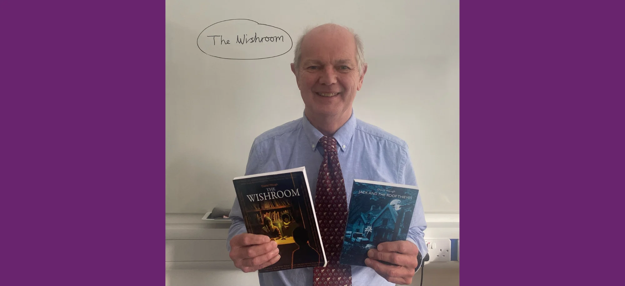 Professor David Waugh standing in front of a whiteboard holding two books he has written.