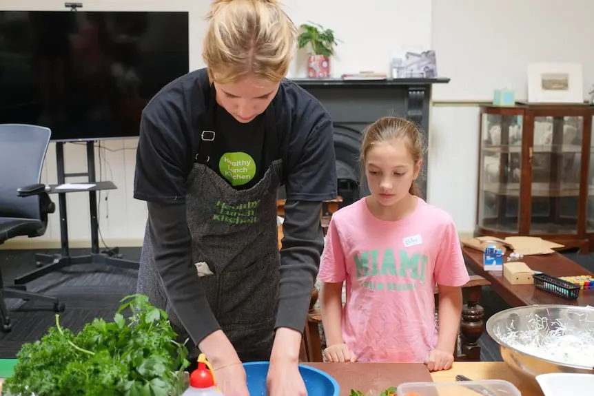 A teenager helps a young girl make rice paper rolls.