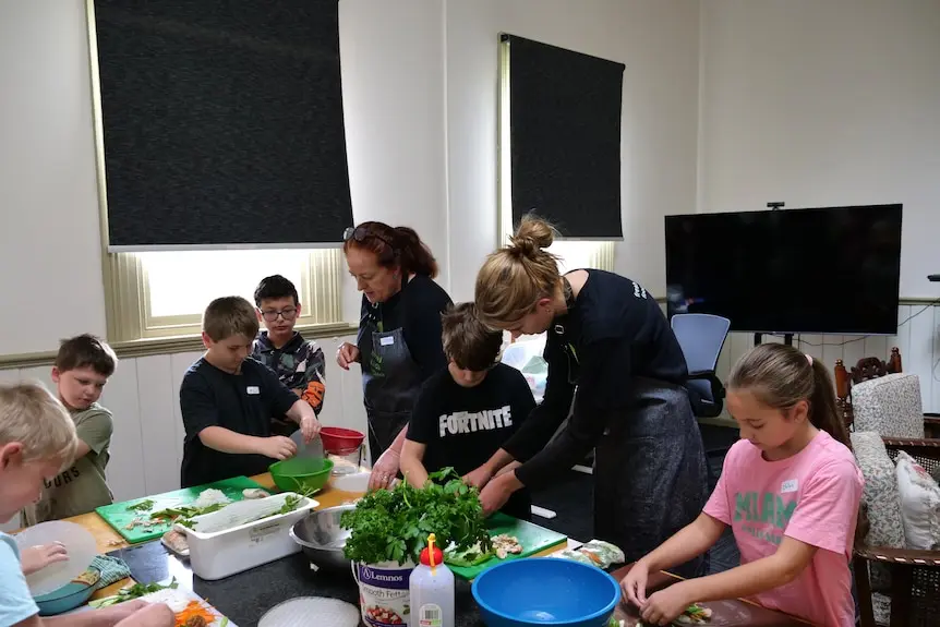 Kids around a table making rice paper rolls.