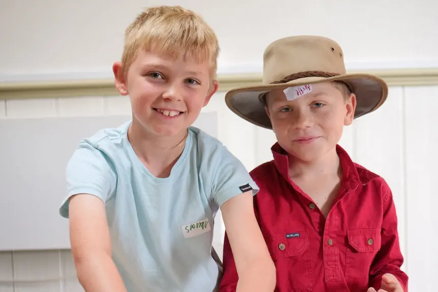 Two boys look at the camera, one has their hands in a mixing bowl.