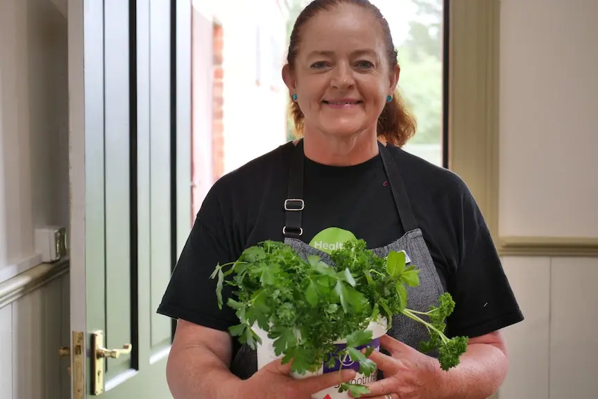 A woman holds a tub filled with herbs and smiles.