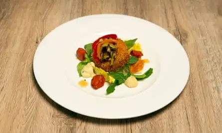 Tuna fish cake sits on some salad, with chunks of chorizo and some vegetable puree, topped with some vegetables