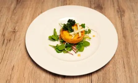 An individual cheese tart, topped with kale, rests on some salad