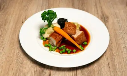 Cubes of pork belly on a plate with vegetables, black pudding and gravy