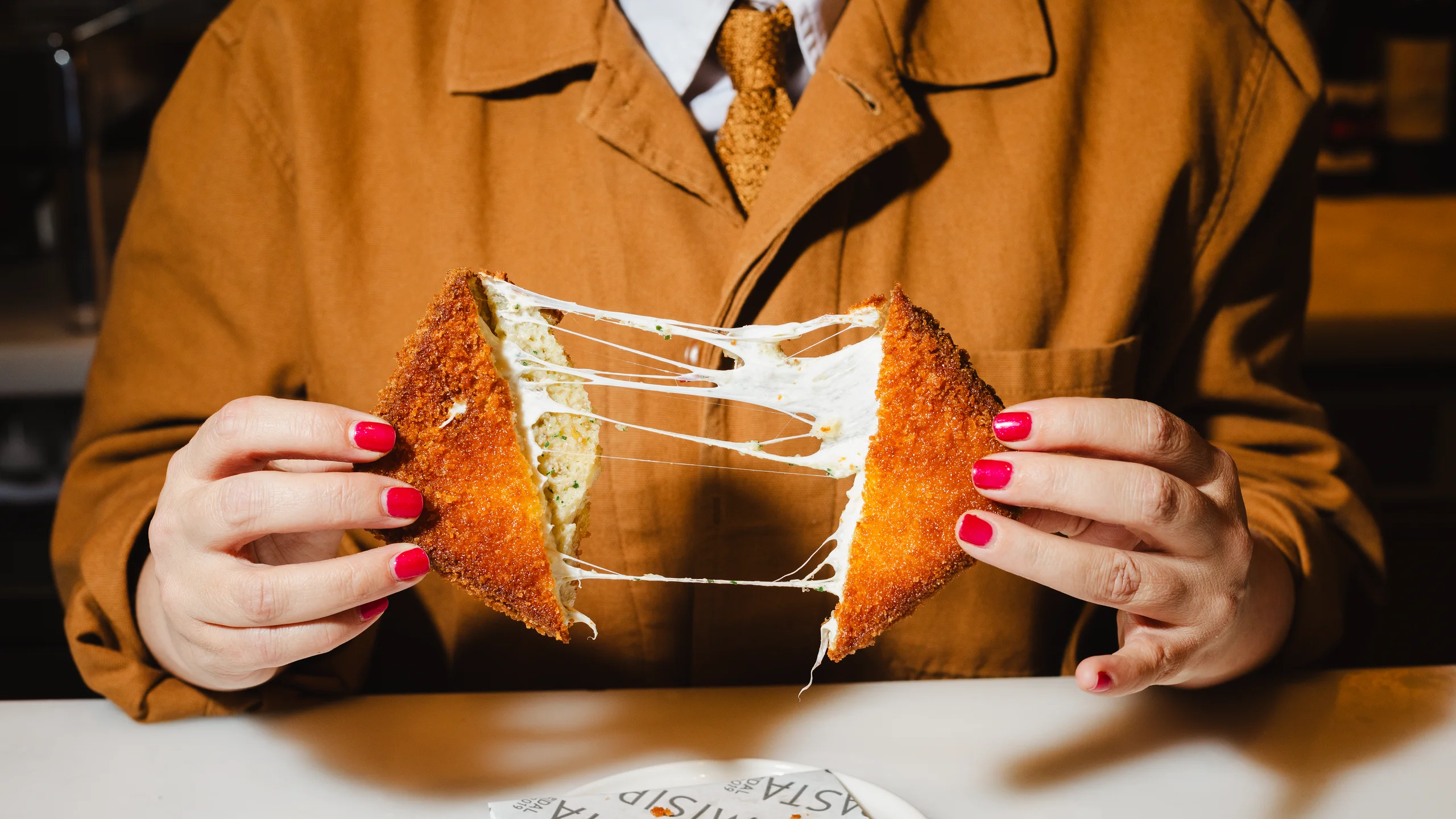 A photo of two hands pulling apart a sandwich with melted strings of mozzarella.