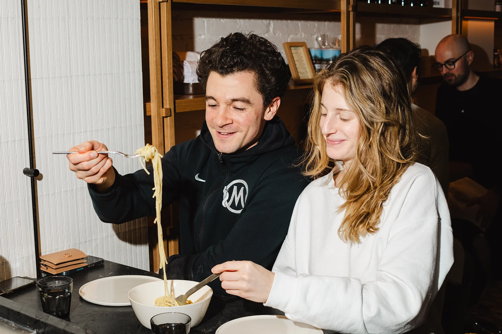 Two people eating pasta together at a table.