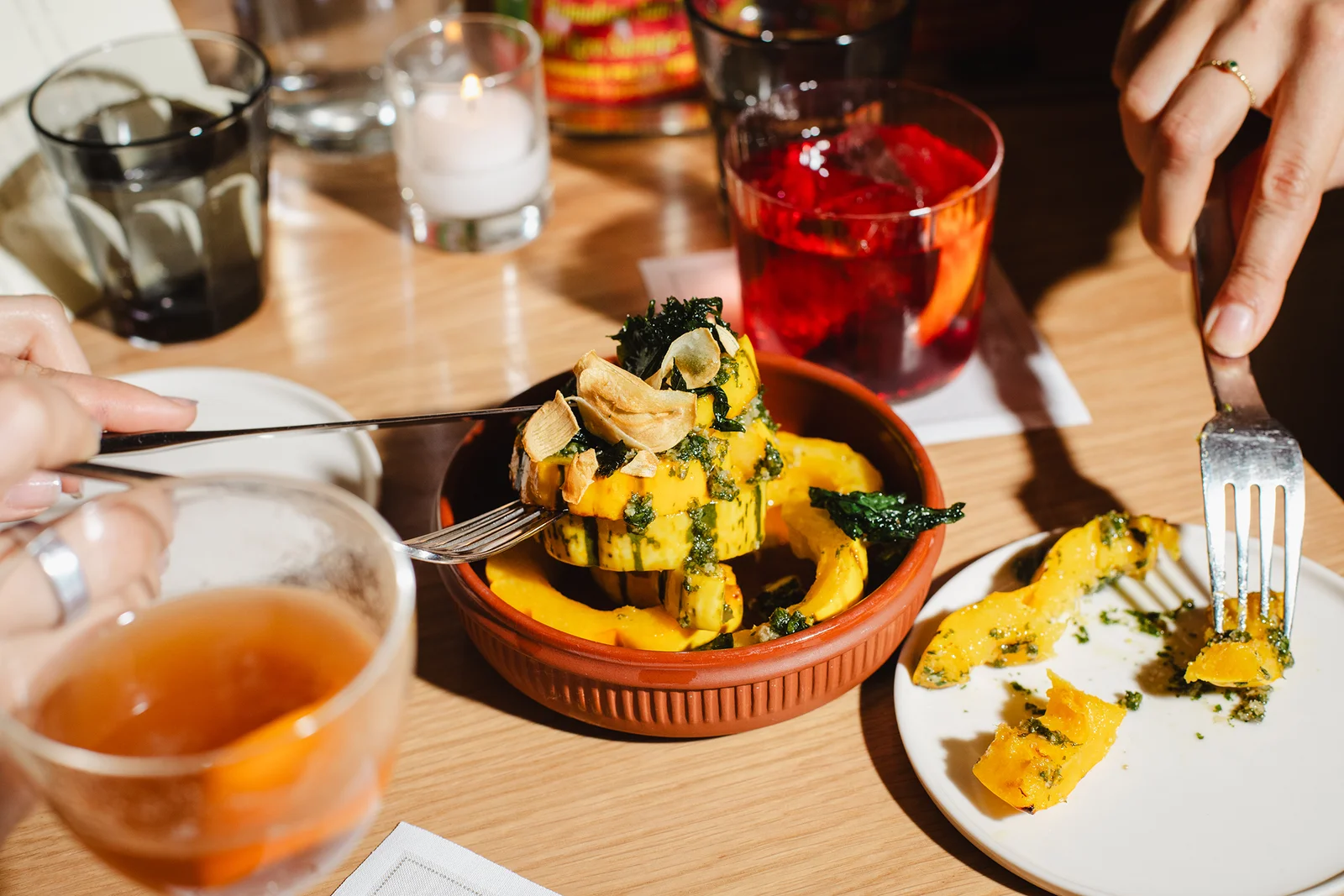 Diners eating a bowl of delicata squash alongside cocktails.