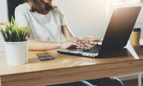 Woman working from home on laptop at desk with plant