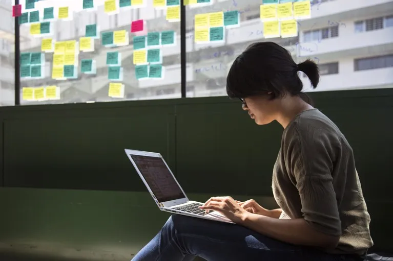 An employee works on a laptop with colourful sticky notes taped to the windows behind