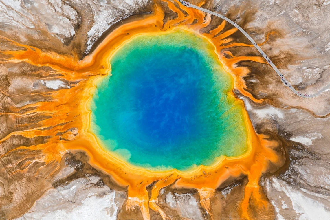 aerial view of Grand Prismatic Spring in Yellowstone National Park, a geyser pool that is deep blue and green in the center and orange and red on the edges, surrounded by arid landscape