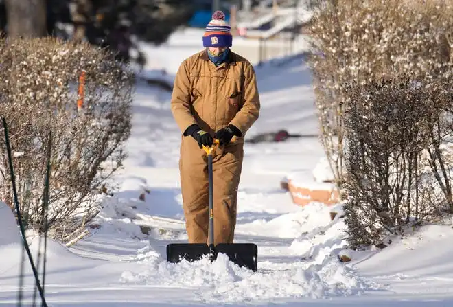 A man clears a light snow from the sidewalk in front of a home in Denver on Jan. 15, 2024