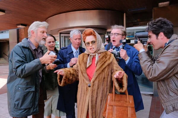 A woman in a fur coat smoking a cigarette stands in the center of a throng of photographers.