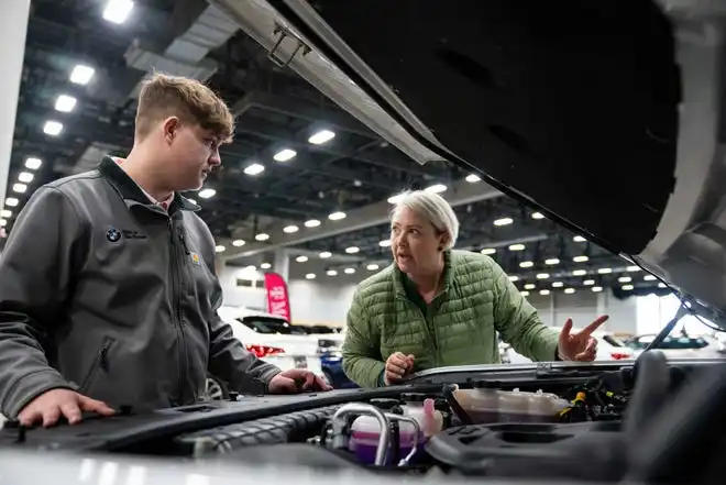 Karsen Shelburg (left) and Brittany Adams (right) of BMW of Des Moines checks under the hood of one of their vehicles Thursday, March 14, 2024, at the Iowa Events Center.