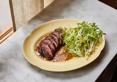 Plate of sliced Hereford onglet with a handful of herbs on a marble counter