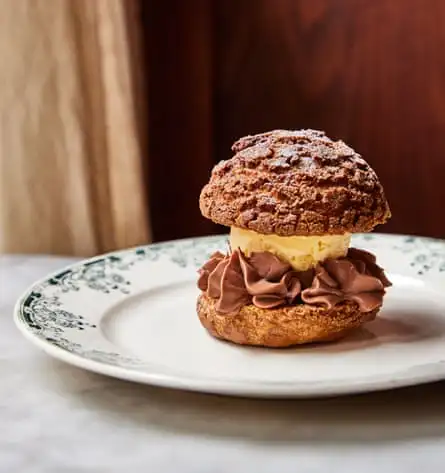 A chocolate bun with ice-cream in the middle and chocolate cream skirted around it