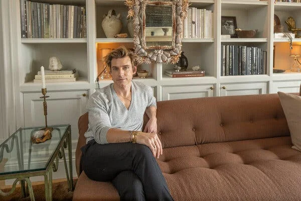 Jeremiah Brent sits on a brown sofa in front of bookshelves he has styled.