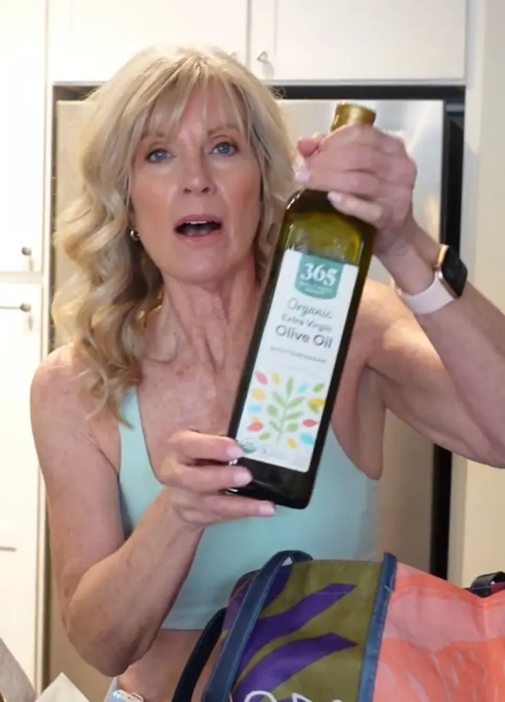 A woman holding a bottle of heart healthy olive oil in her grocery basket.