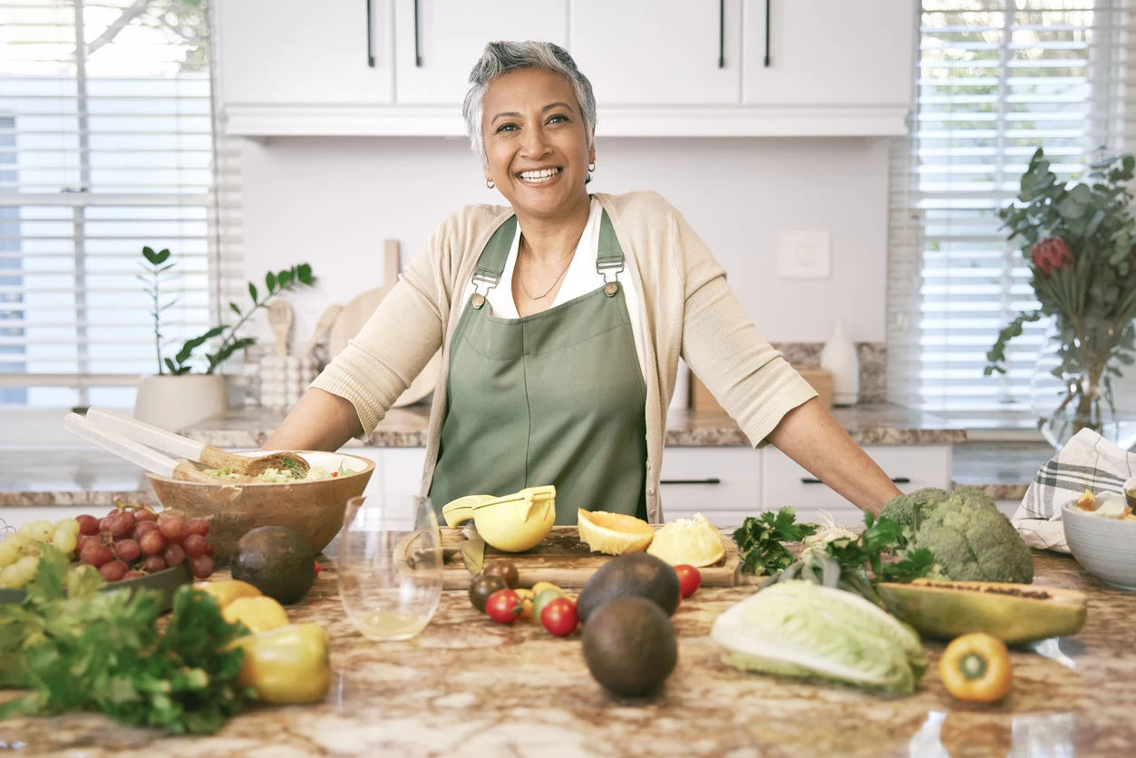 Woman standing at kitchen counter preparing healthy food smiling at camera