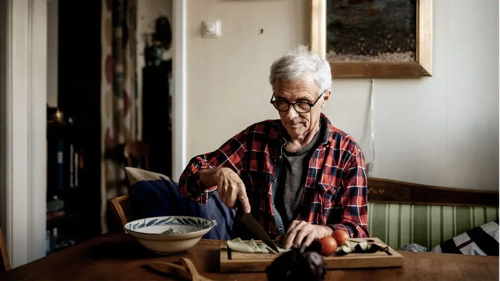 older main in plaid shirt slicing vegetables