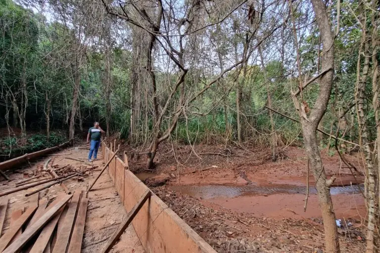 Image shows a man standing on a bridge with a small stream flowing by