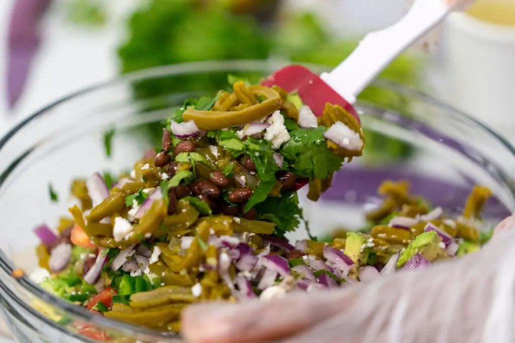 A person is stirring a salad with a spatula. Participants will learn how to cook healthy foods using fresh fruits and vegetables at the Do Well, Be Well with Hypertension program beginning April 3 in Waco. 