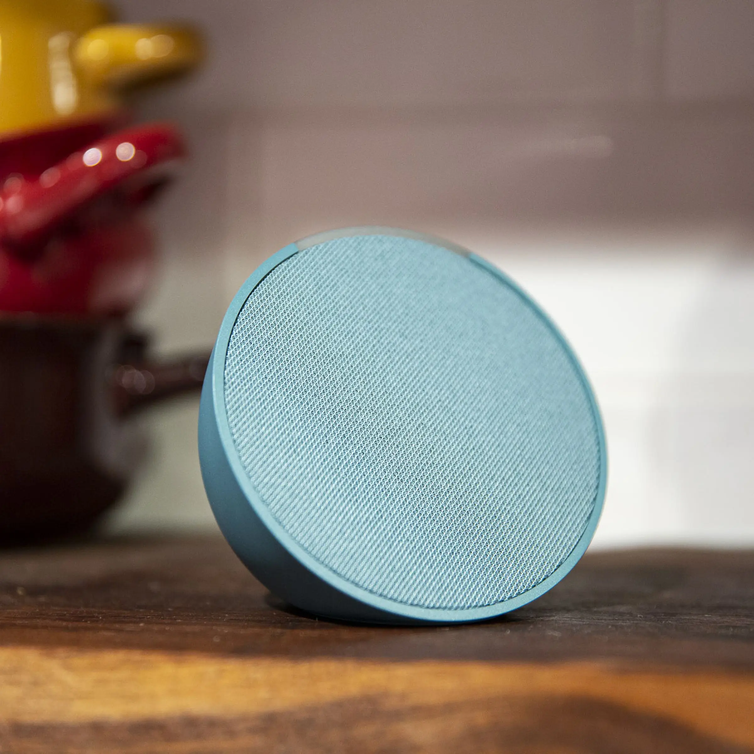 Teal Amazon Echo Pop viewed at an angle with colorful pots in the background.