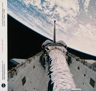 a shiny spacecraft rests in the white cargo bay of a space shuttle with a large swath of earth in the background.