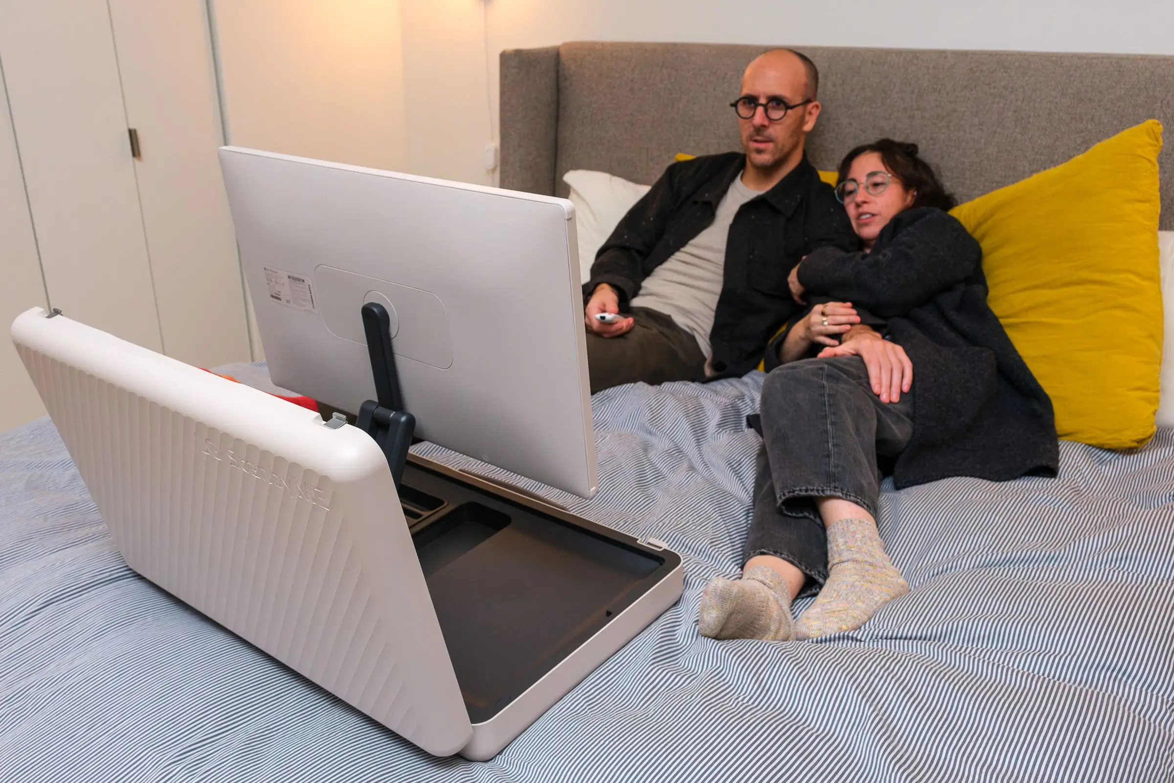 A photo of a couple laying in bed watching LG’s StanbyME Go briefcase TV.