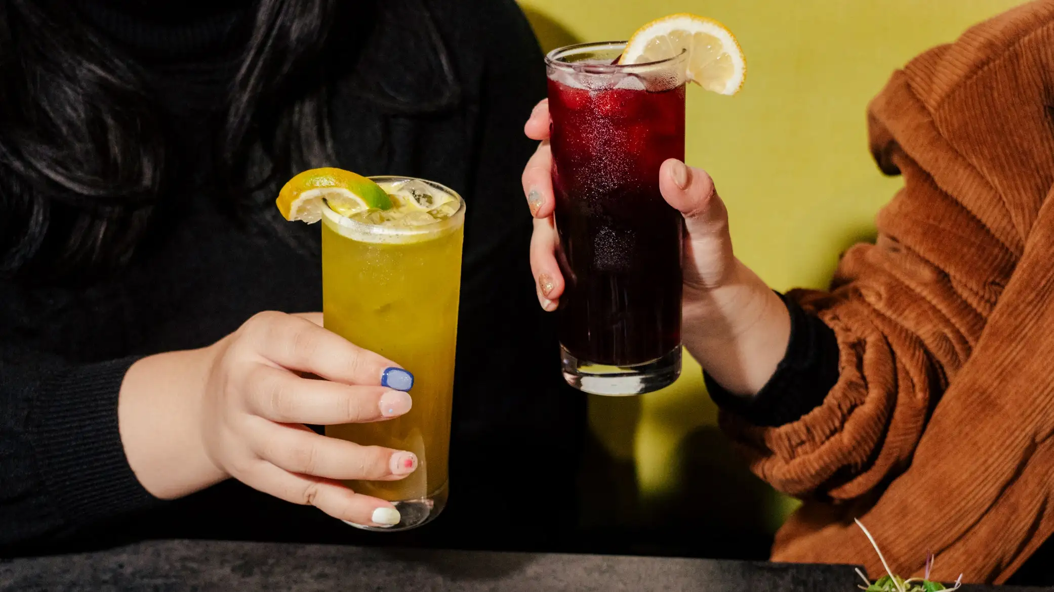 Two diners with colorful beverages in front of a plate of tostones with ceviche.