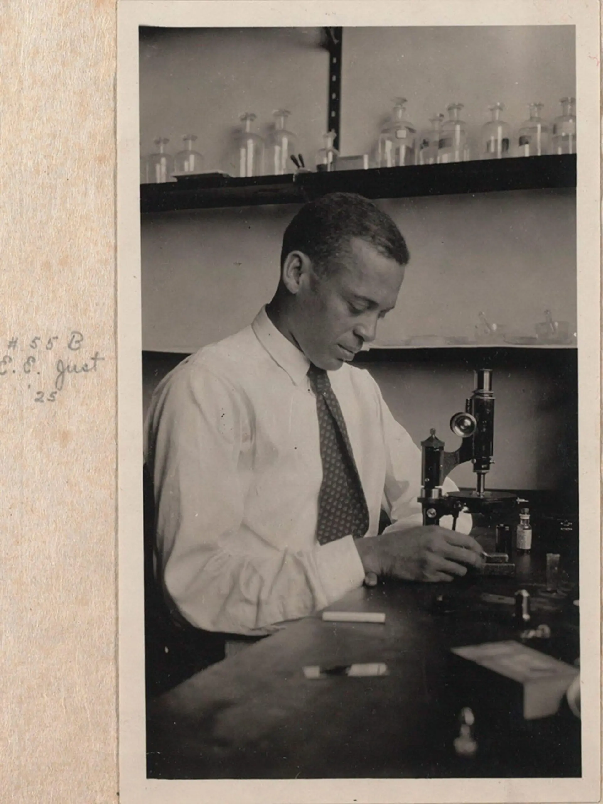 An African American scientist at work in a lab with a microscope. The image is an older print within a photo album