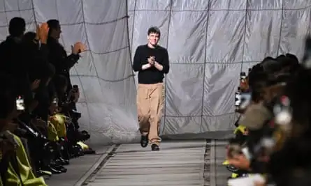 Members of the audience on both sides of the runway applaud Seán McGirr and hold up their phones to take pictures