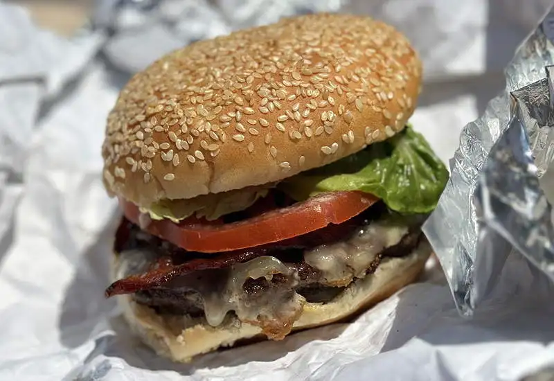 A burger with lettuce, tomato, and cheese on a seeded bun on a sheet of foil wrap