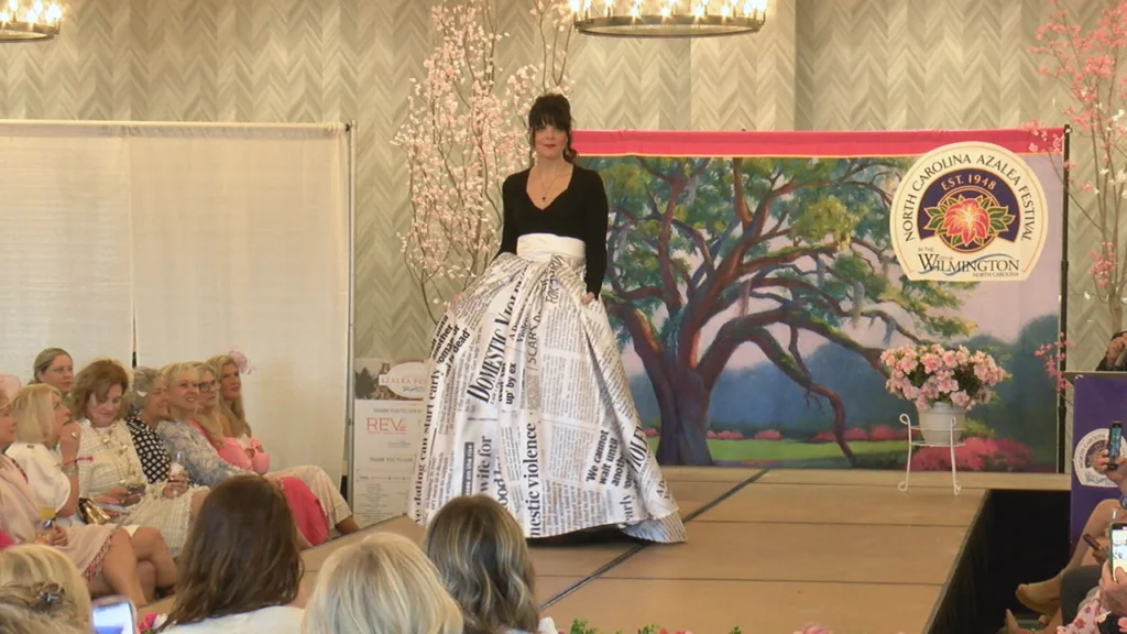 Executive Director of Operation Pretty Things Missy Bennett walks the runway in a custom gown. The skirt is comprised of newspaper headlines and articles relating to domestic violence. (Photo:Nate Mauldin/WWAY News)