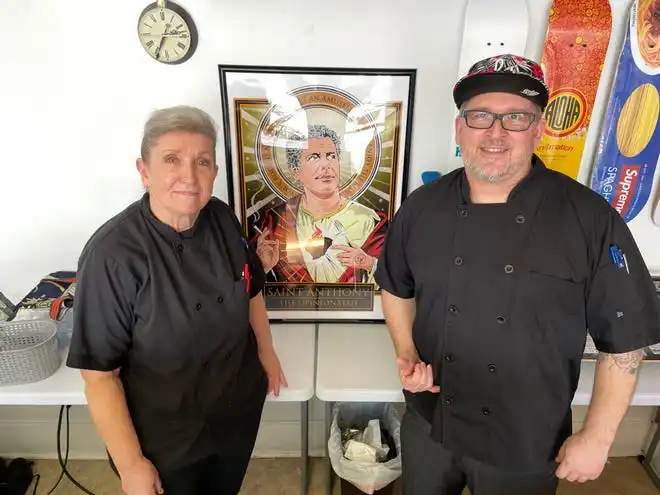 Cathy Watson and her son Colin Canale stand beside a whimsical poster of celebrity chef Anthony Bourdain at their new restaurant, Canale's Deli, in Martinez, Ga., April 2, 2024.