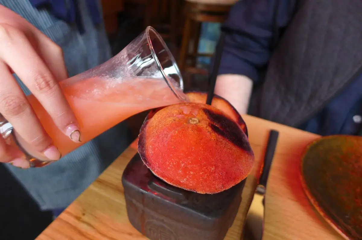 A hand pours liquid from an orange flask into a frozen and singed orange peel.