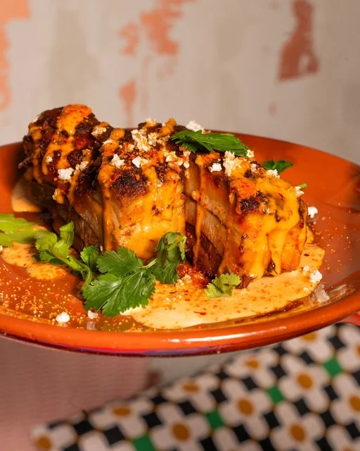 Photo of a plate of pork belly, against a tiled floor.