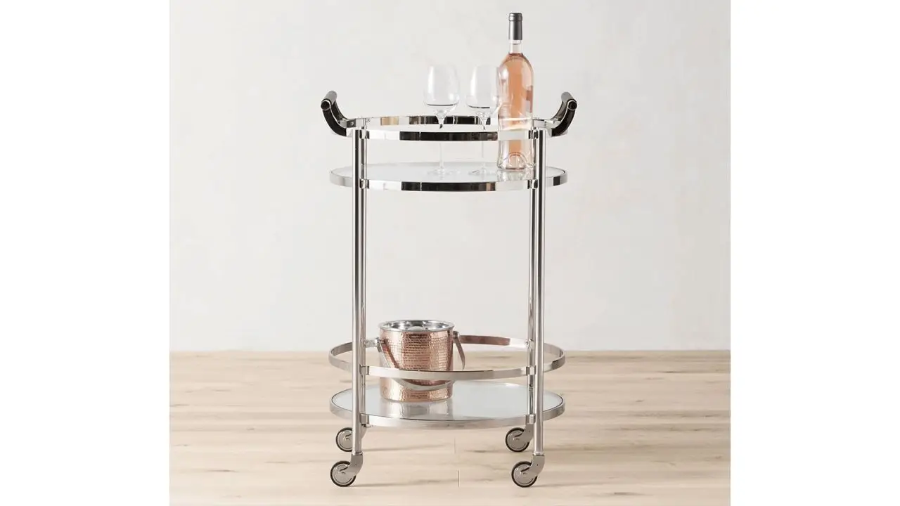 The Williams Sonoma Truman Round Bar Cart with a bottle of wine and two glasses on its top shelf and an ice bucket on its bottom shelf.