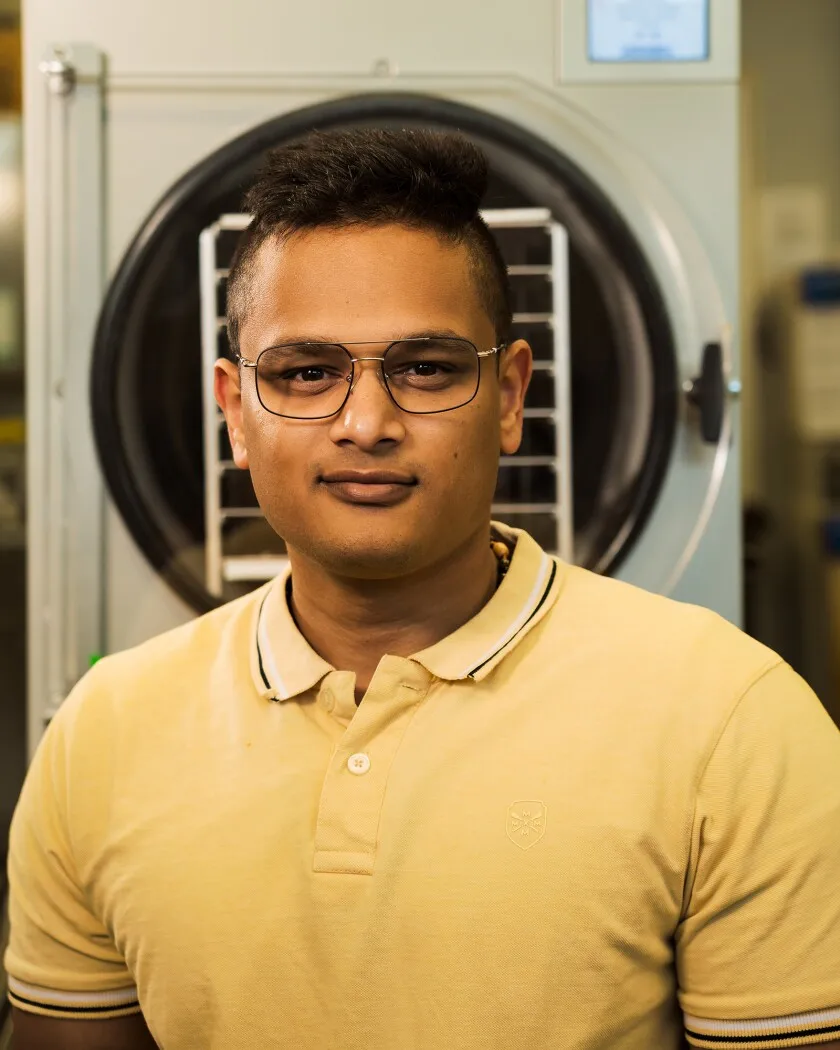 An Indian man in a yellow shirt stands in front of a grey machine.