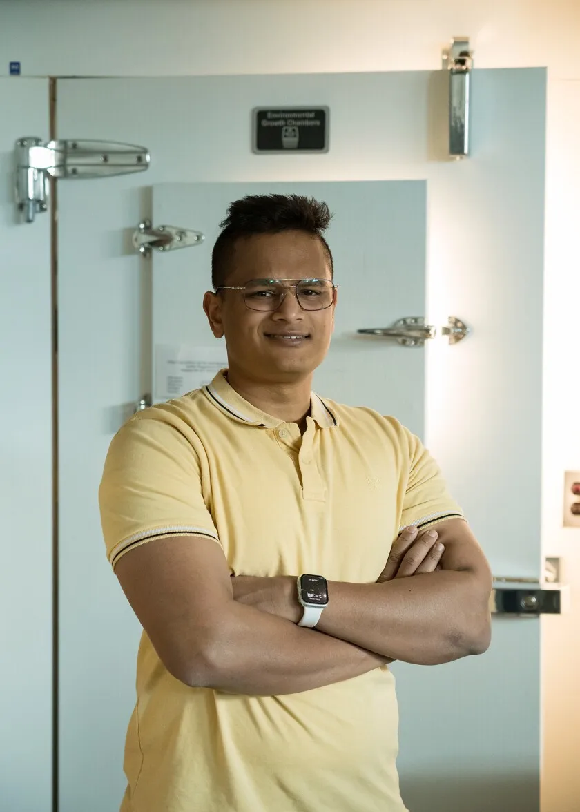 An Indian man in a yellow shirt stands in front of a light grey freezer door. 