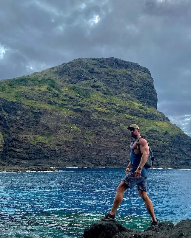 a man standing on a rock by a body of water with a mountain in the background a man standing on a rock by a body of water with a mountain in the background