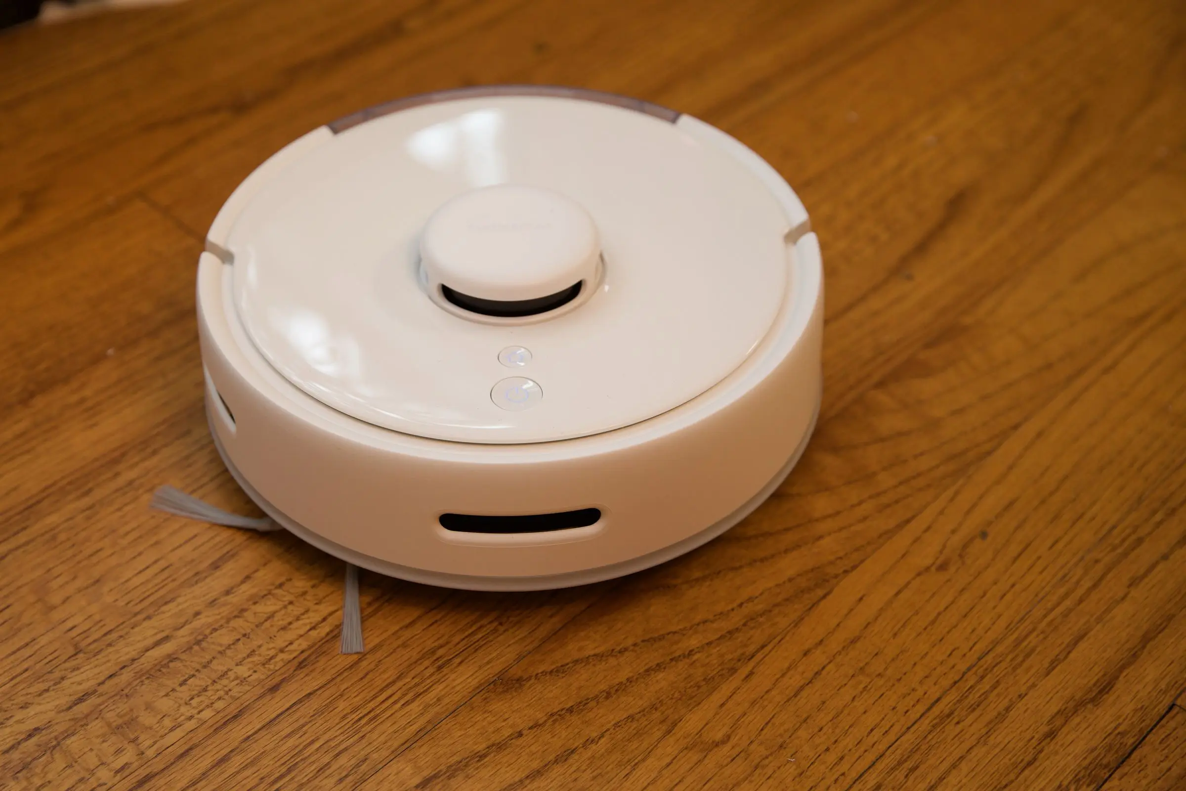 A white robot vacuum on a hardwood floor.