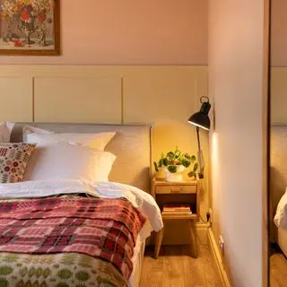 Bedroom with double bed and colourful blankets, bedside tables and lamps, green curtains